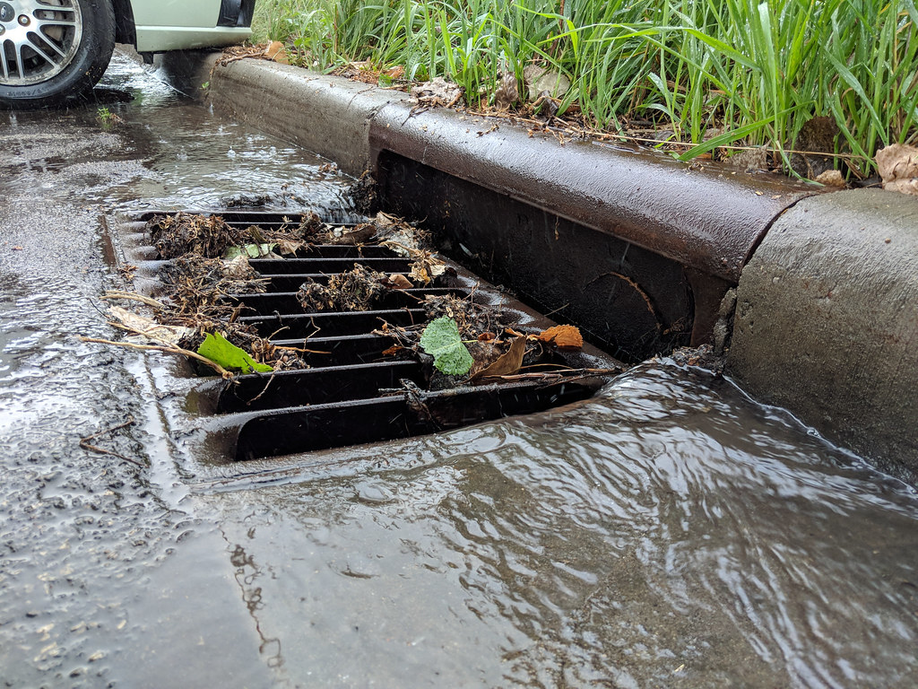 Clogged street drain with debris and flowing water