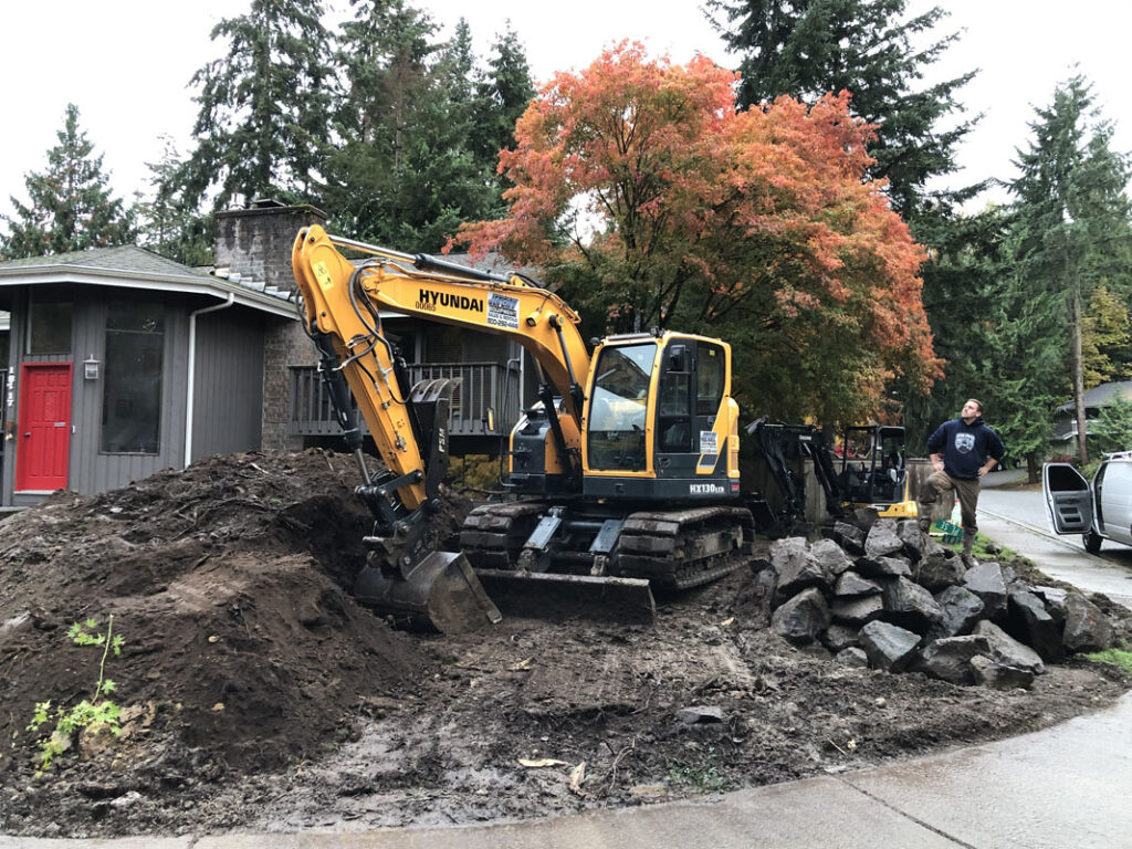 Excavator digging soil near house with autumn trees