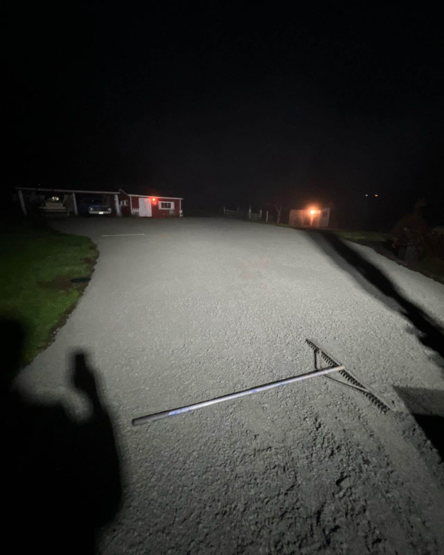 Nighttime view of a driveway with a rake on asphalt