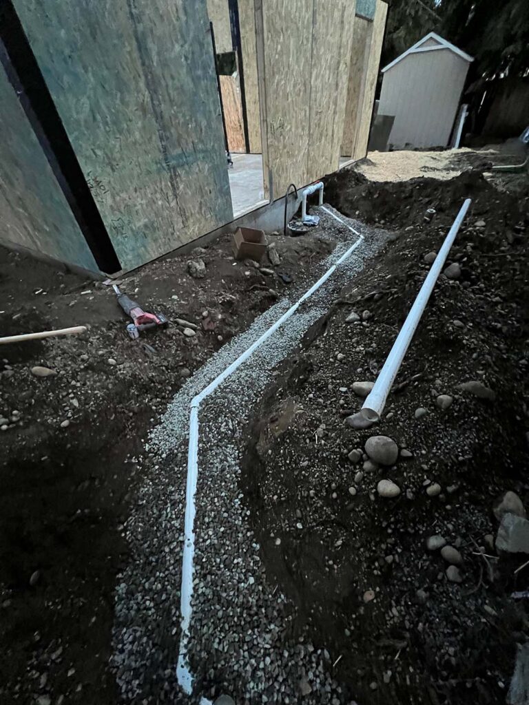 Trench with PVC drainage pipes beside building