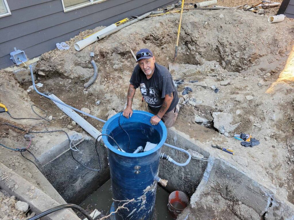 Man installing blue water tank in excavation pit